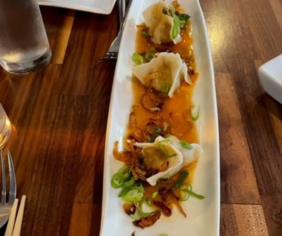 Picture of three wontons with a brown sauce on a white plate
