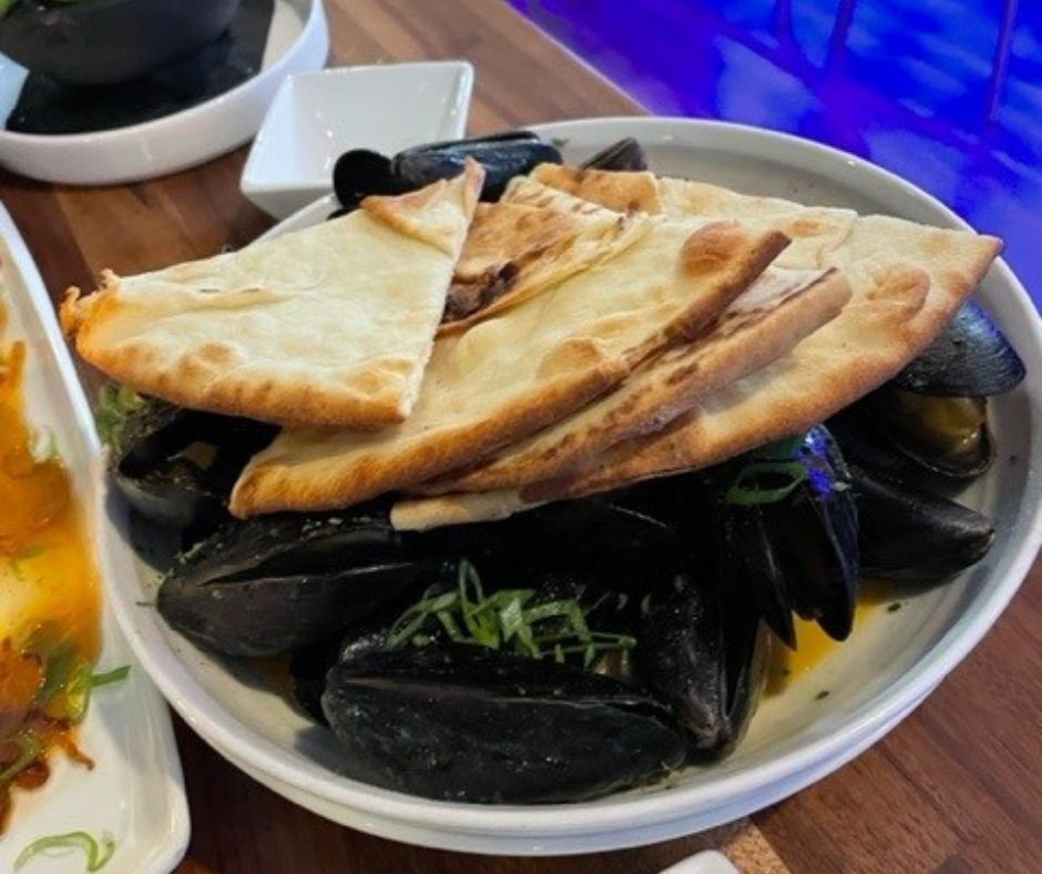 Bowl of mussels with four slices of pita bread on top