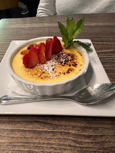 Creme Brulee wotj a sprig of mint and sliced strawberries on a square plate with a silver spoon