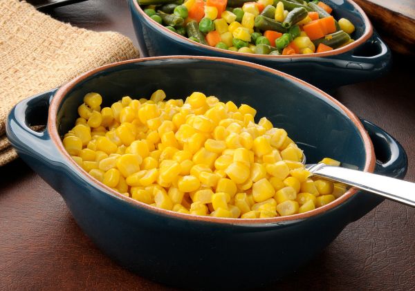 Bowl of corn with a spoon in it, another bowl with mixed veggies
