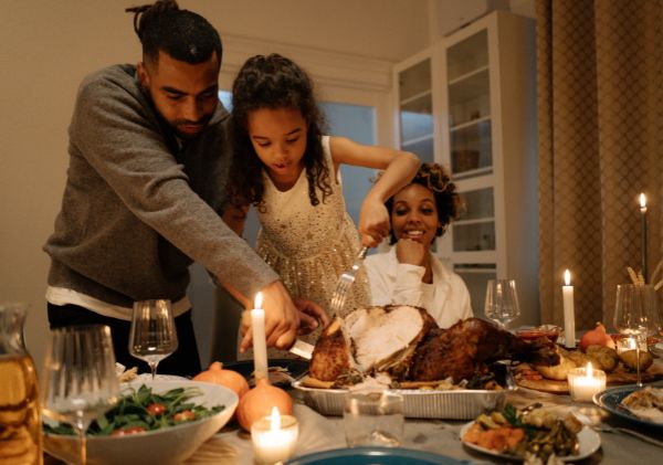 Two adults watching/helping a young girl cut the turkey