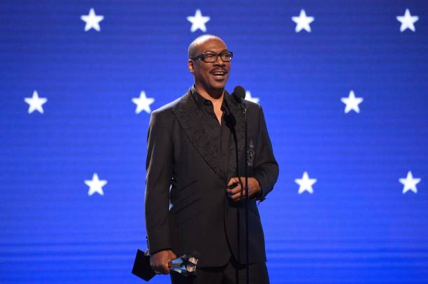 Picture of Eddie Murphy in a black suit in front of a blue background with white stars