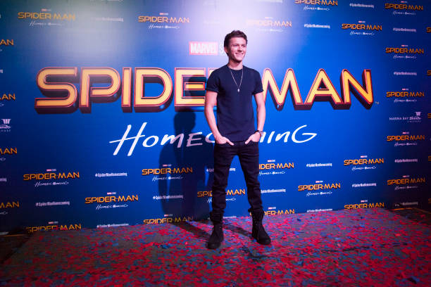 Tom Holland standing in front of a Spider-Man Homecoming sign