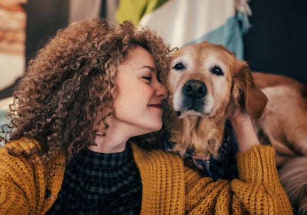 Woman with curly hair snuggling an older dog