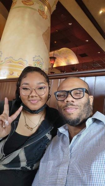Picture of a Black father and his young adult daughter holding up a peace sign.