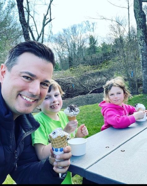Picture of a father, his young son, and young daughter sitting at a picnic table eating ice cream