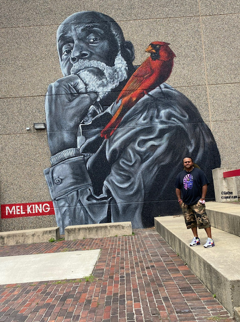 Mural of legendary Boston activist Mel King with his fist under his chin and a red cardinal on his shoulder. In the bottom right is the artist GoFive. 