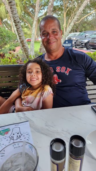 Father in a Red Sox shirt sits at a table with his smiling daughter