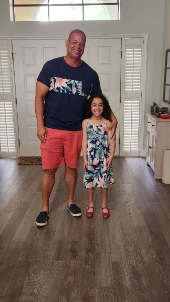 Man in a navy shirt and coral color shorts. Daughter wearing a print dress that matches a piece of her father's shirt