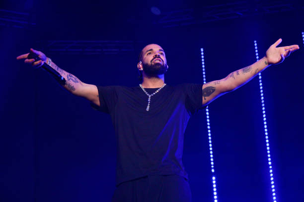 Picture of Drake on stage with his arms open, wearing a black shirt and pants