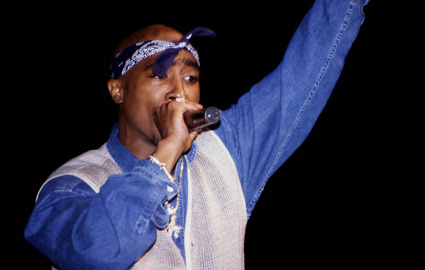 Picture of Tupac with a microphone in his hand. Blue bandana around his head, blue shirt with a white vest