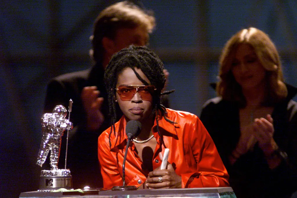 Lauryn Hill in an orange satin top with her awards and orange sunglasses