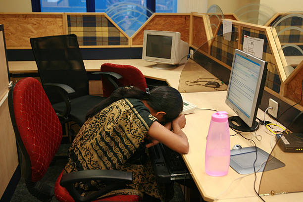 Person sitting at a desk with head down falling asleep in front of a computer.