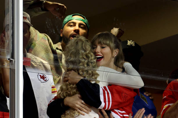 Taylor Swift hugging a woman with blonde wavy hair at the Chiefs game.