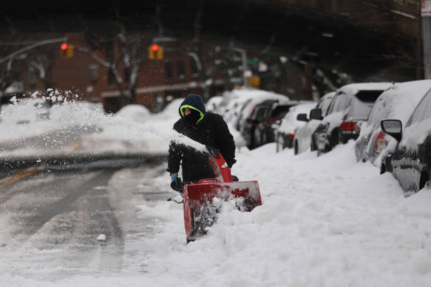 A person operates a snow plow on the side of the street