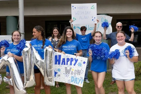 Group of people wearing blue Make-A-Wish shirts and carrying signs that say Happy Wish Day.