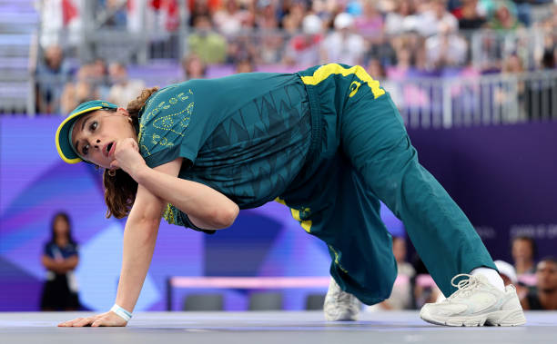 Australian break dancer Rachael Gunn in a green and yellow shirt, pants, and hat. She's positioned twisted on the ground. Olympic-themed Halloween costumes.