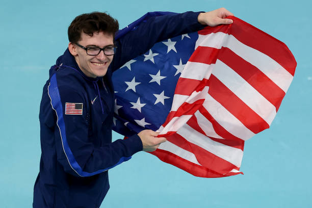 Bronze medalist Stephen Nedoroscik from the Men's Gymnastic Olympic team smiling and holding a US Flag to the side. 